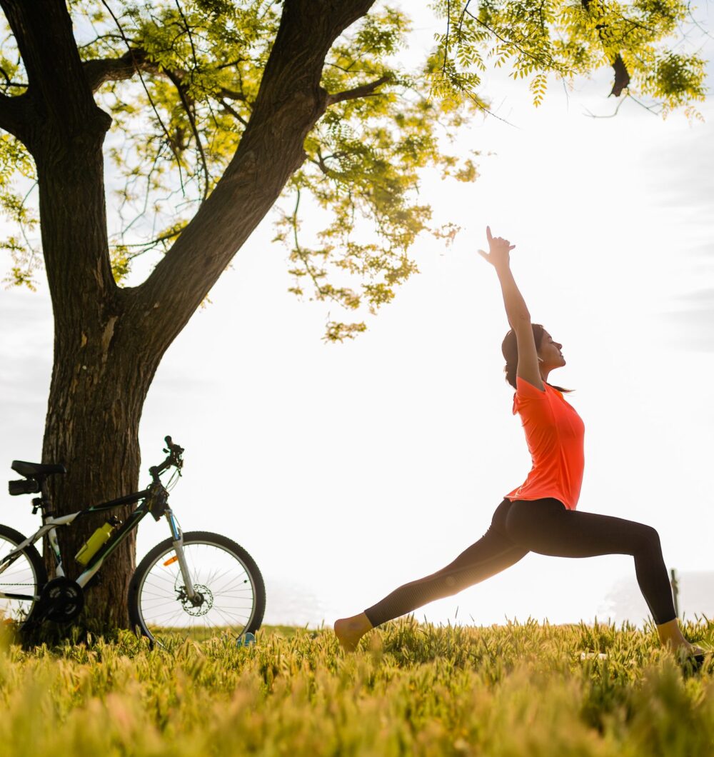 slim beautiful woman silhouette doing sports in morning in park doing yoga on mat in colorful fitness outfit in nature, smiling happy healthy lifestyle, calm meditation, bicycle on background